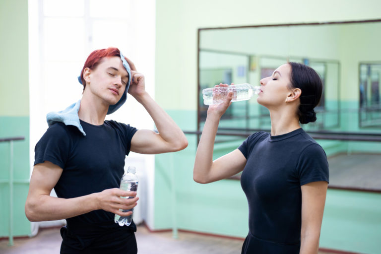 A young boy dancer and young girl dancer drink water during class in a studio.