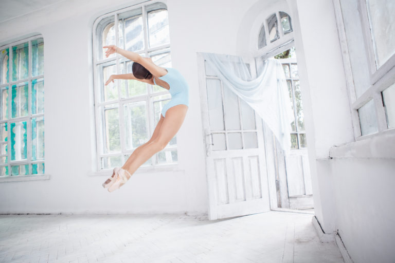 young modern ballet dancer jumping or flying on white room background