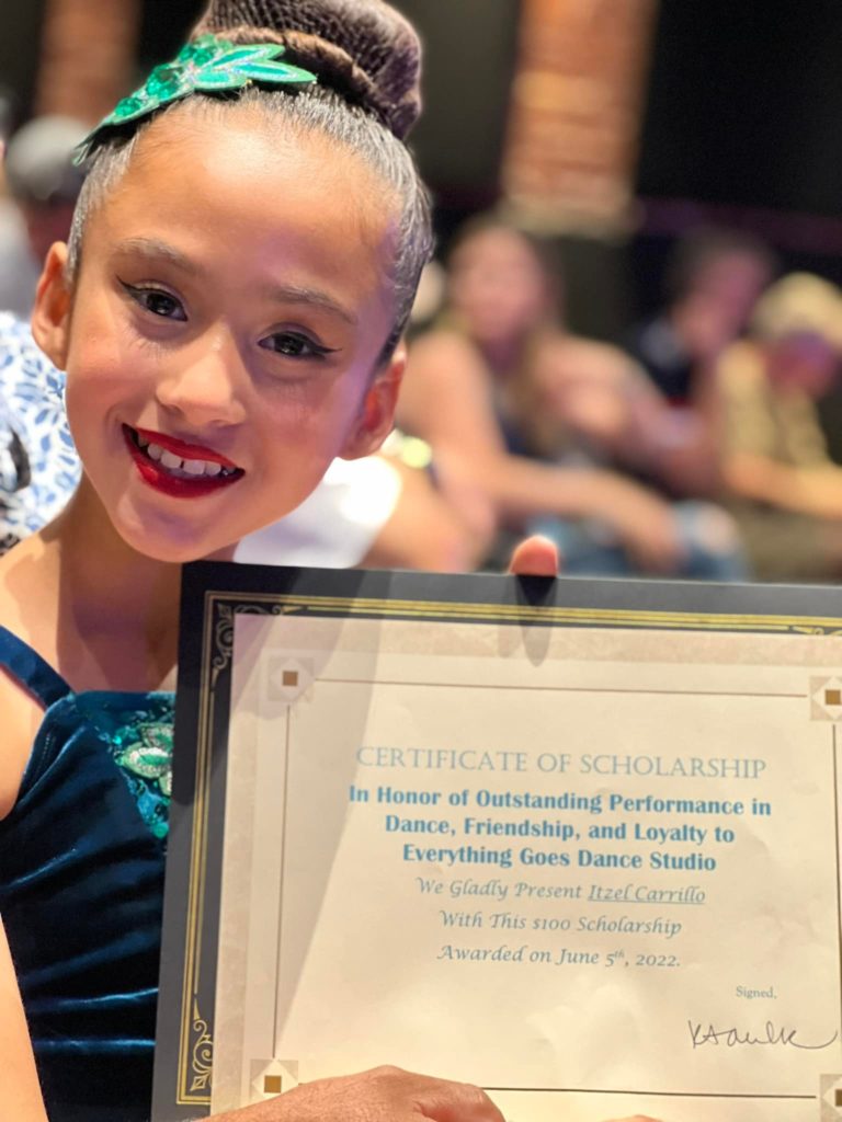 A young dancer holds a framed certificate.
