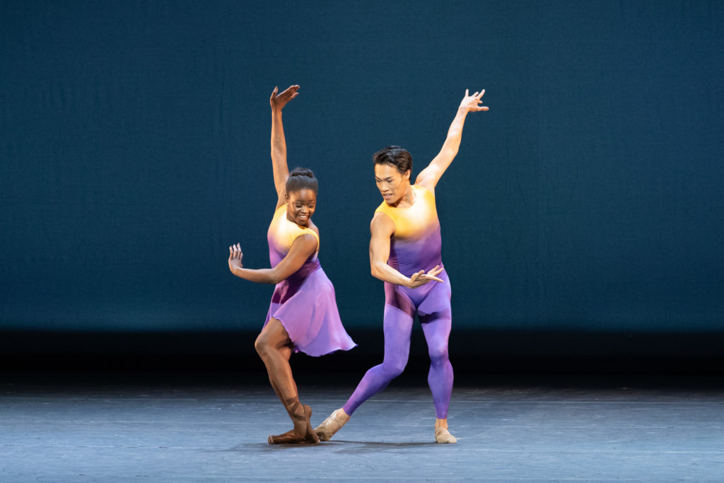 A ballerina and a male ballet dancer, both wearing purple and gold costumes, dance on stage.