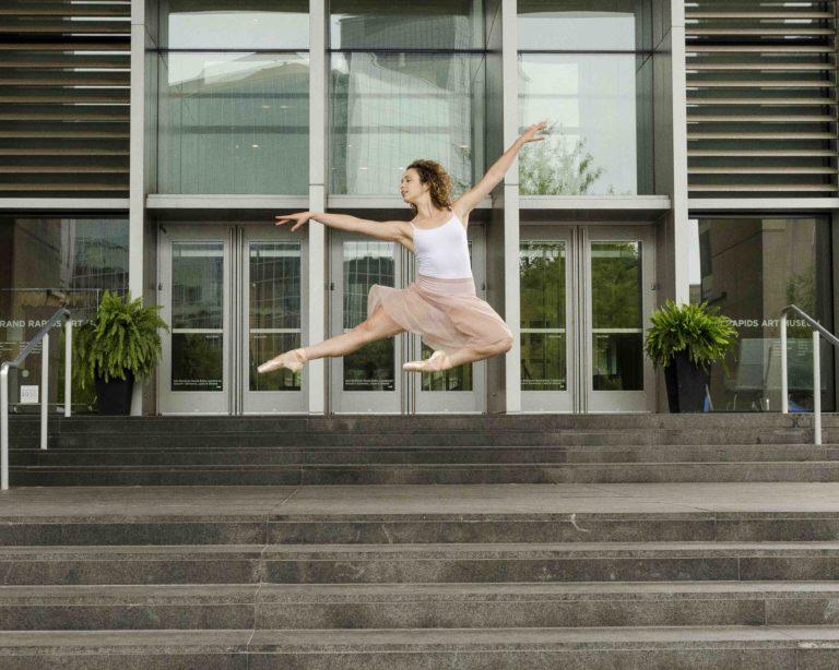 Image of ballerina leaping in front of a performing arts facility