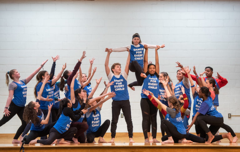 Image of DEL students performing onstage wearing t-shirts that read "Dance for every child"
