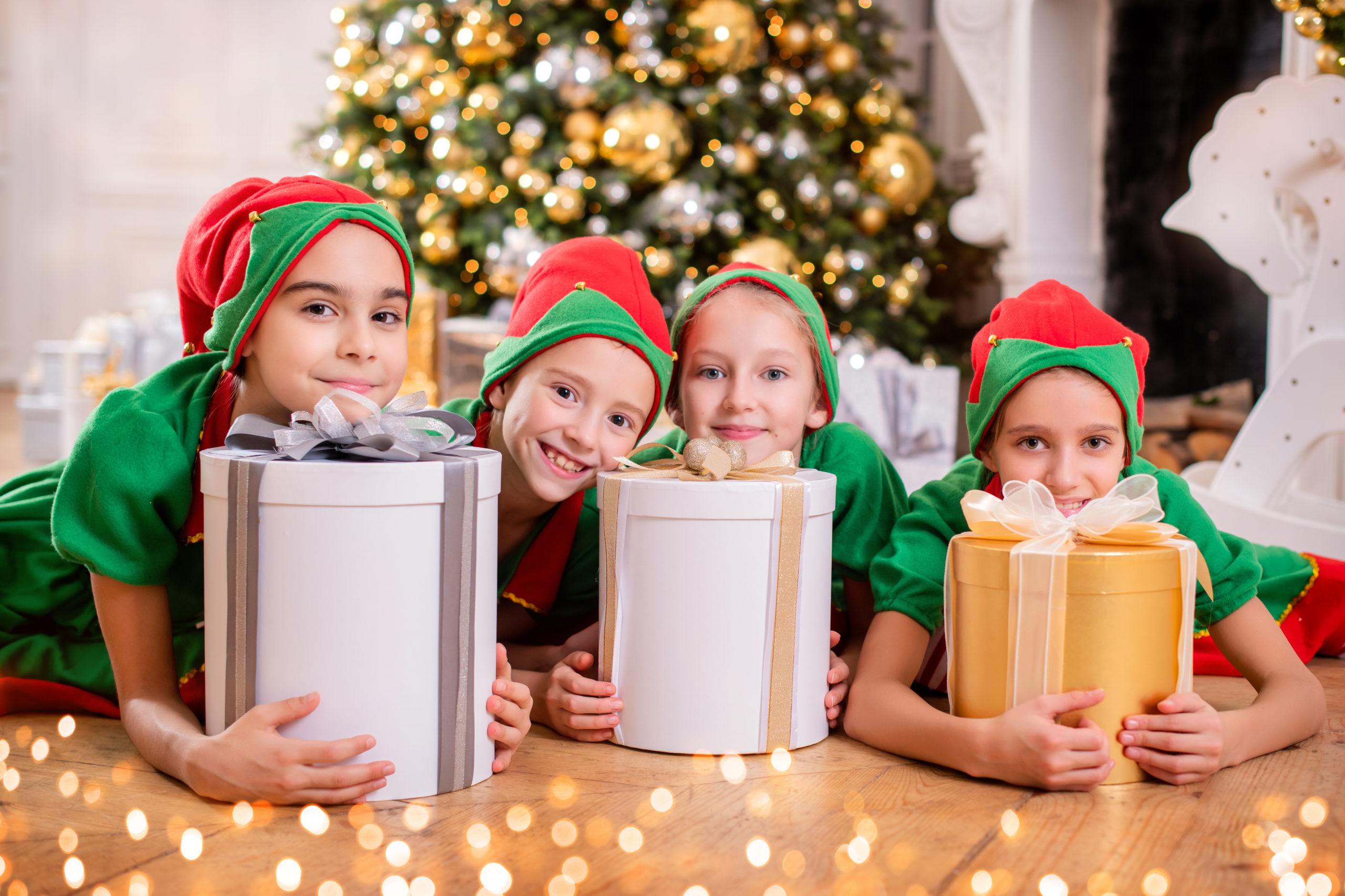 Group of cheerful happy children in costumes of elves with gifts on background of Christmas tree