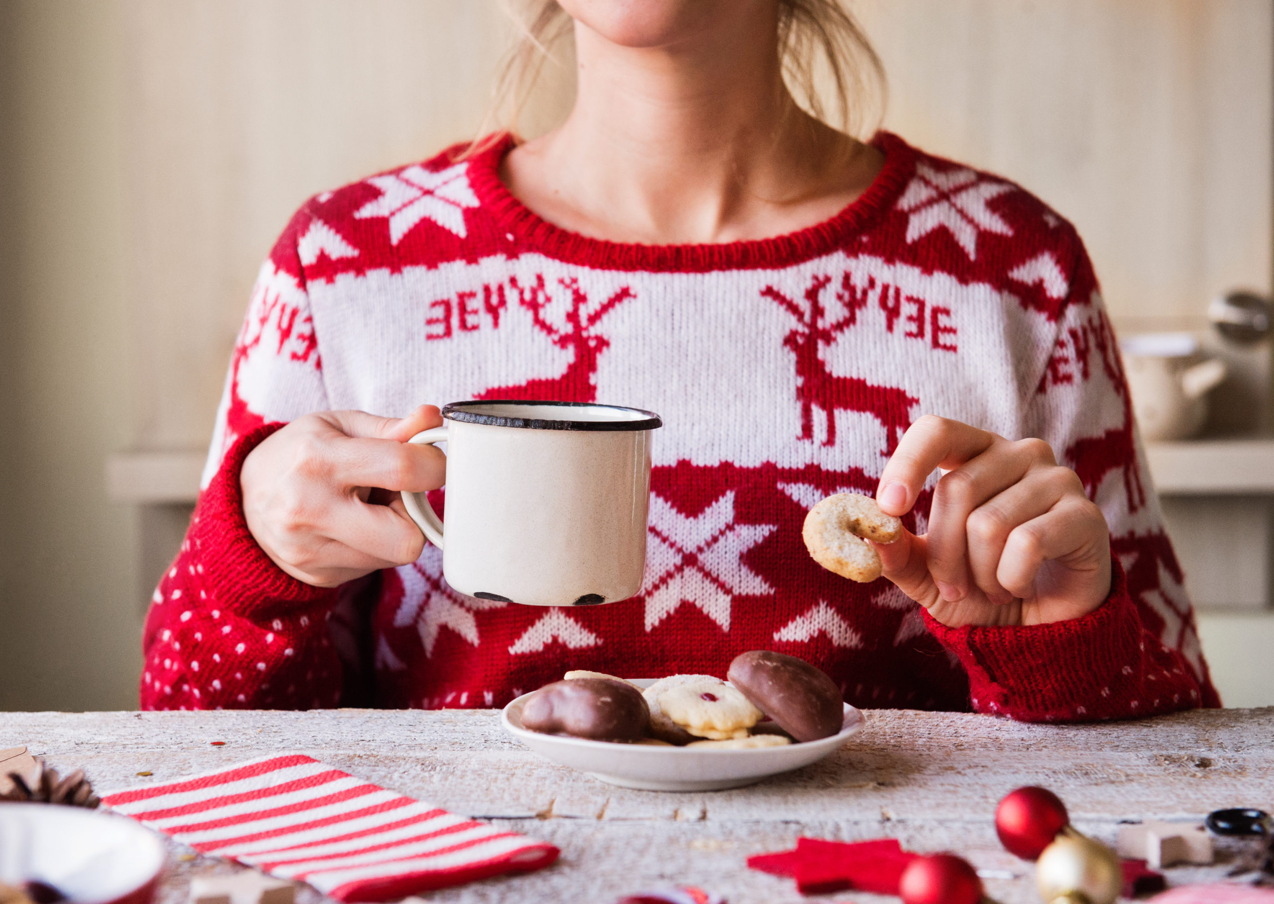Woman wearing a holiday sweater eating biscuits and drinking coffee.