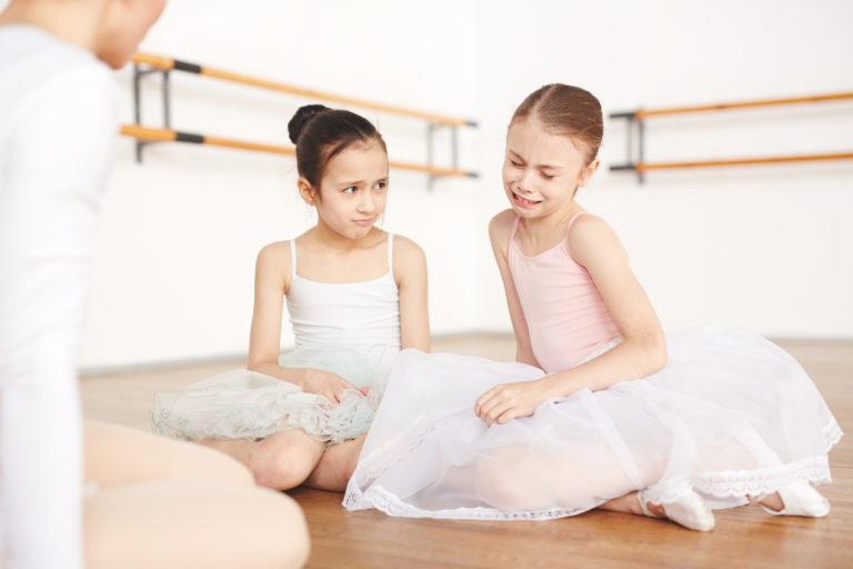 Little sad ballet students sitting on floor in studio