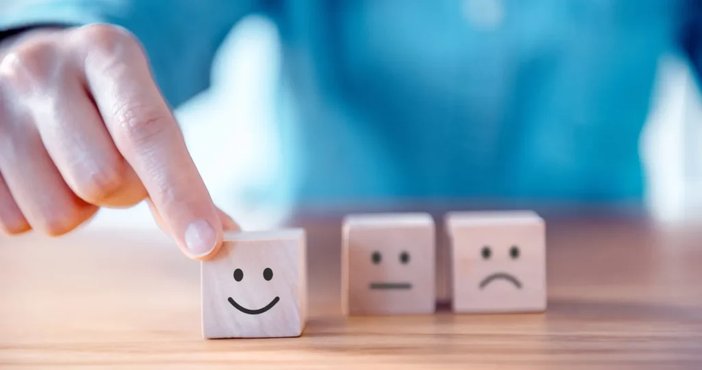 3 wooden blocks with smiling and sad faces. The smiling block is held and moved forward.