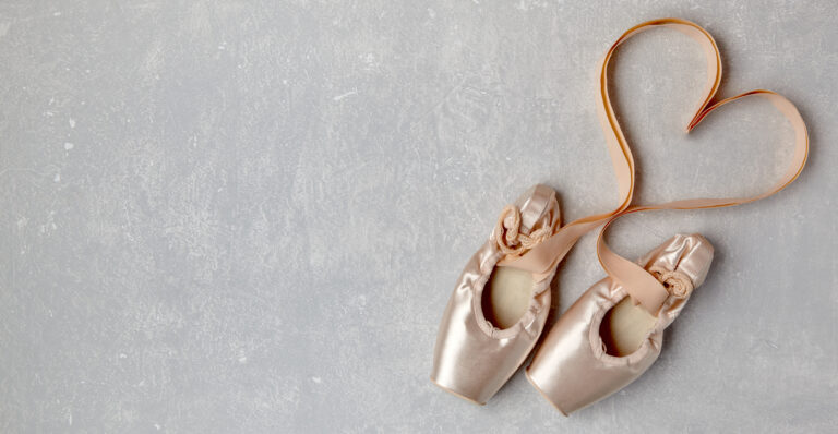 Beige pointe shoes with ribbons laid out in the shape of a heart