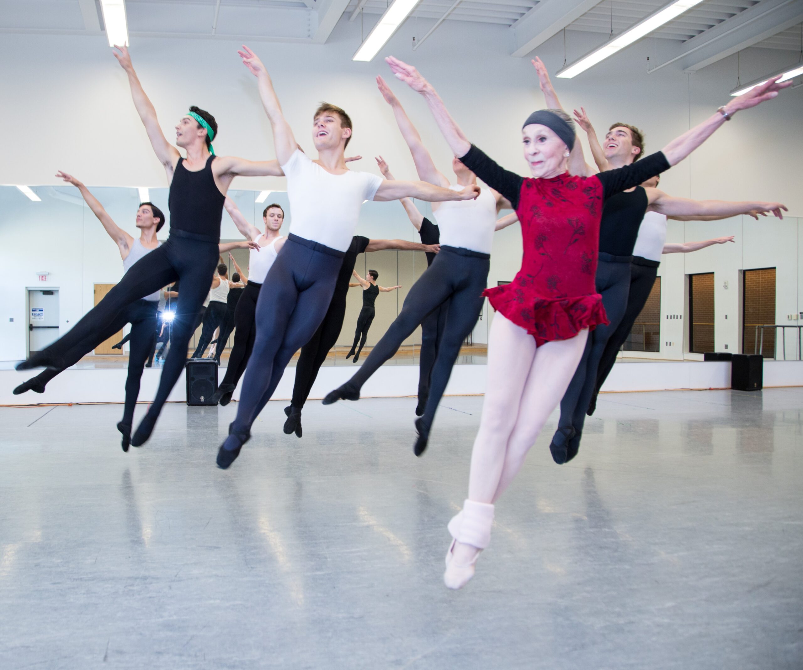 Image of older dance educator jumping with young male dancers in a dance studio.