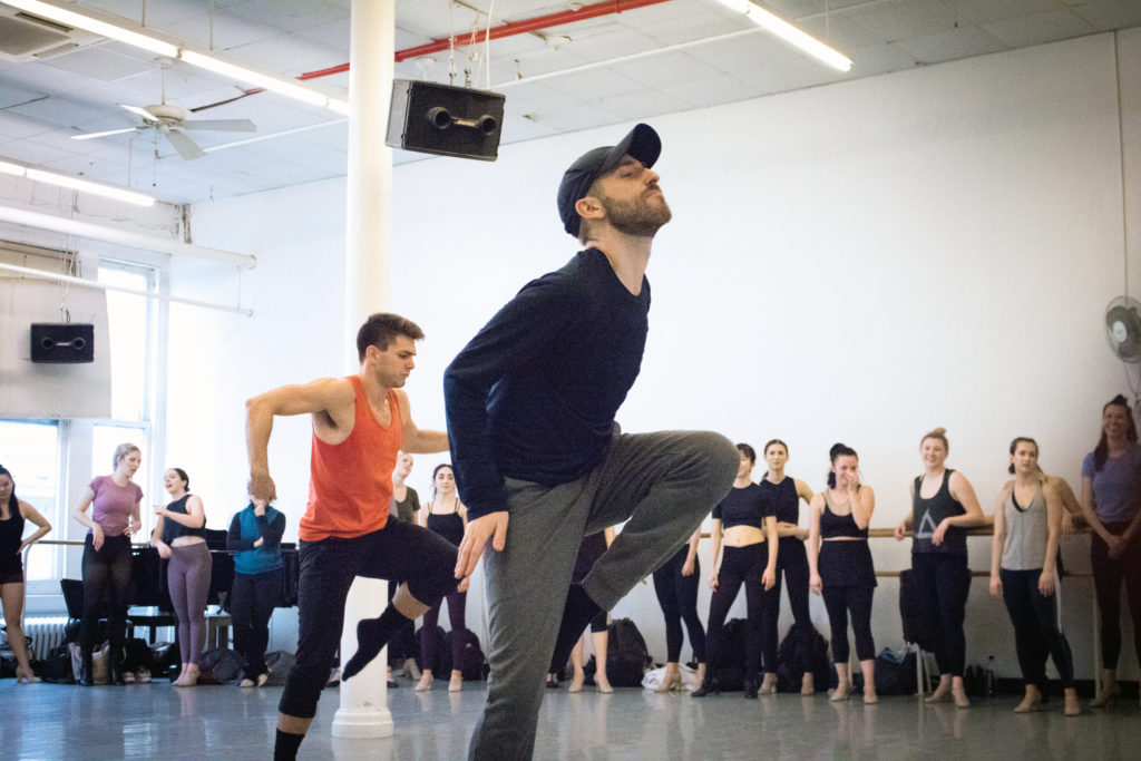 In a long sleeve black shirt, gray athletic pants and a black baseball cap, BIlly Griffin leads an energetic dance class in a brightly lit studio.