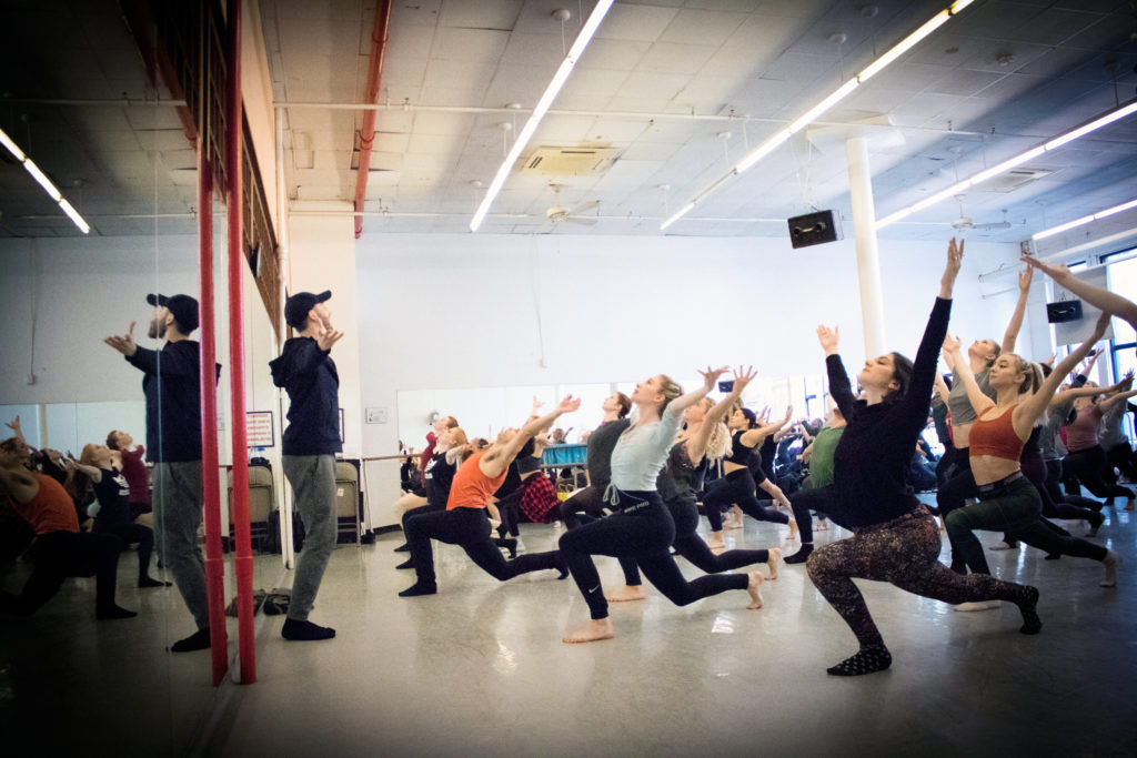 In a long sleeve black shirt, gray athletic pants and a black baseball cap, BIlly Griffin leads an energetic dance class in a brightly lit studio.