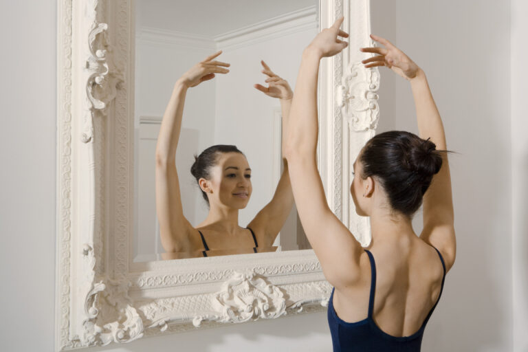 Ballerina posing in front of mirror with arms in 5th position.