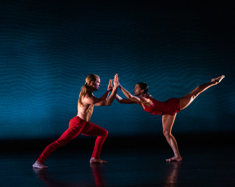 Jacqueline Burnett and David Schultz dancing together on stage wearing red costumes.