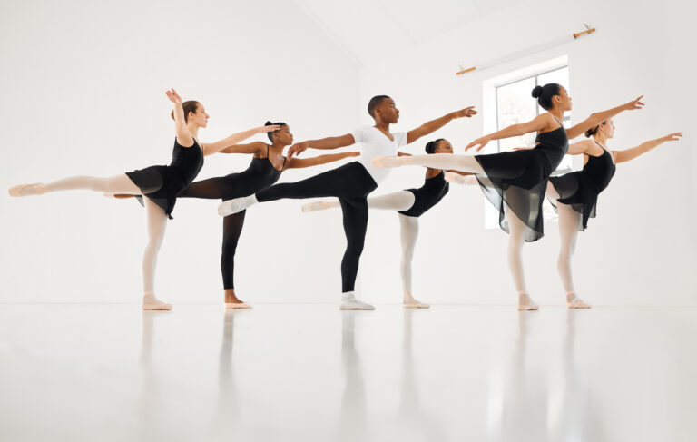 A group of ballet studentds practicing arabesque in a studio.