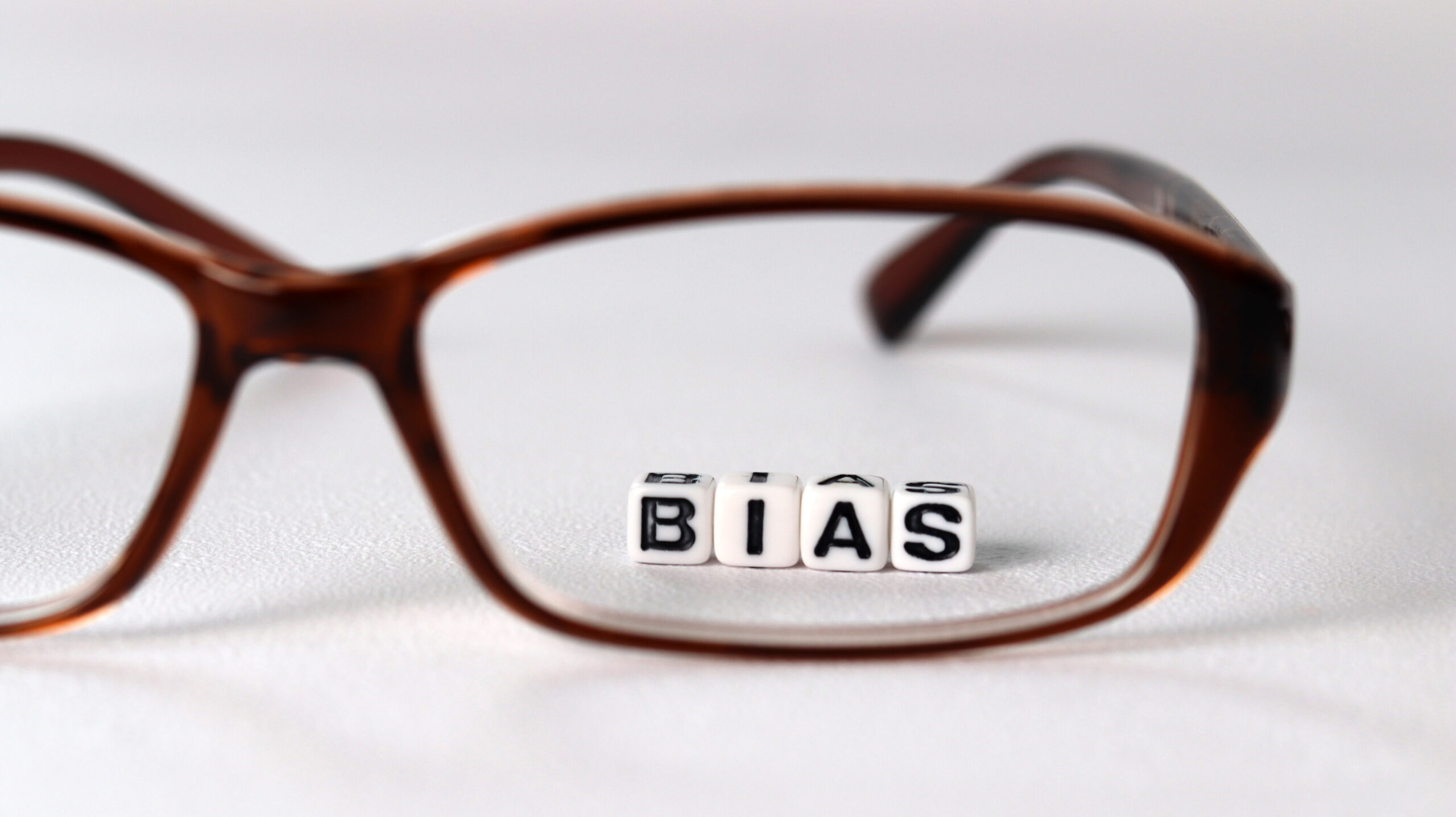 Stock photo of beads reading "bias" behind a pair of glasses.
