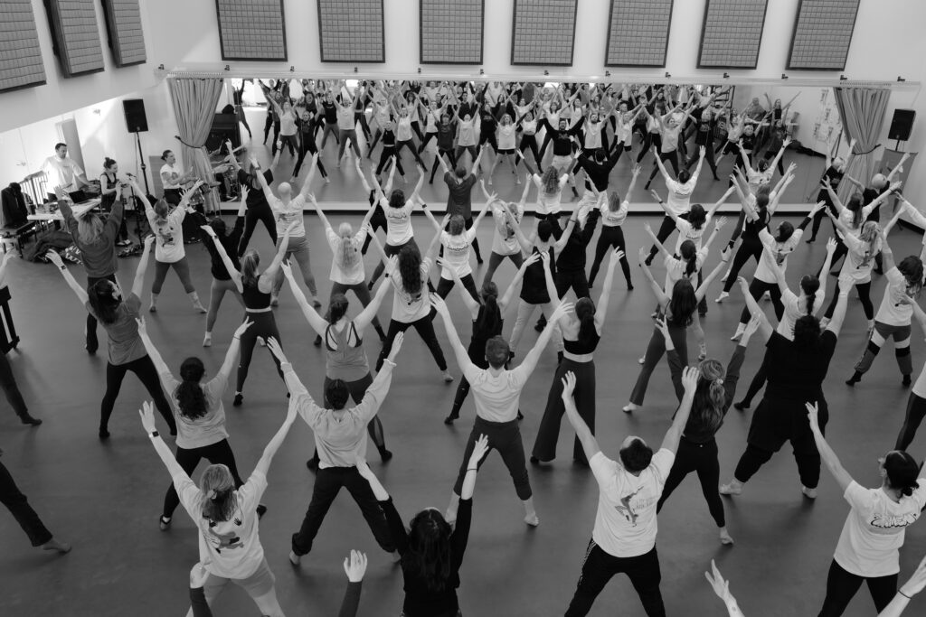 Black and white photo of a big group of dancers with their arms in the air.