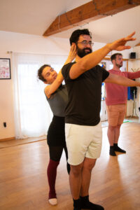Studio image of Bridgit Lujan in black tights and legwarmers adjusting a student standing in first position.