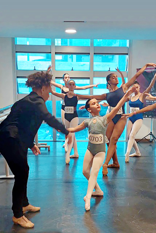 Caridad Martinez working with young ballet dancers wearing blue leotards and tights with numbers on their chests.