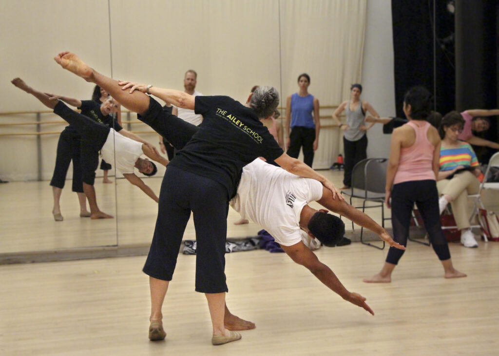 Ana Marie Forsythe guides a young dancer through a Horton lean -- his arms reach towards the floor with one leg up. 