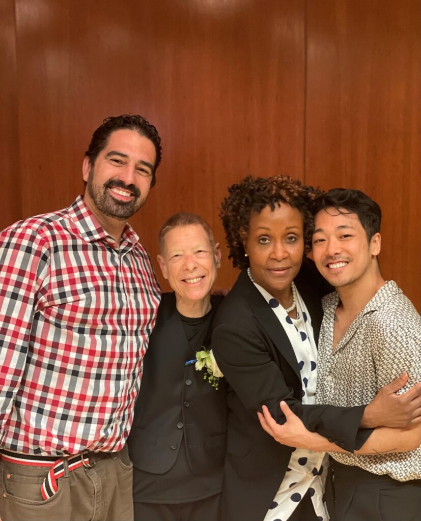 Gregory Youdan, Jr., a tall Latino man; Irene Dowd, an older white woman; Renee Robinson, a Black woman; and Bret Yamanaka, an Asian American man. All four stand close together, arms around each other as they smile at the camera.