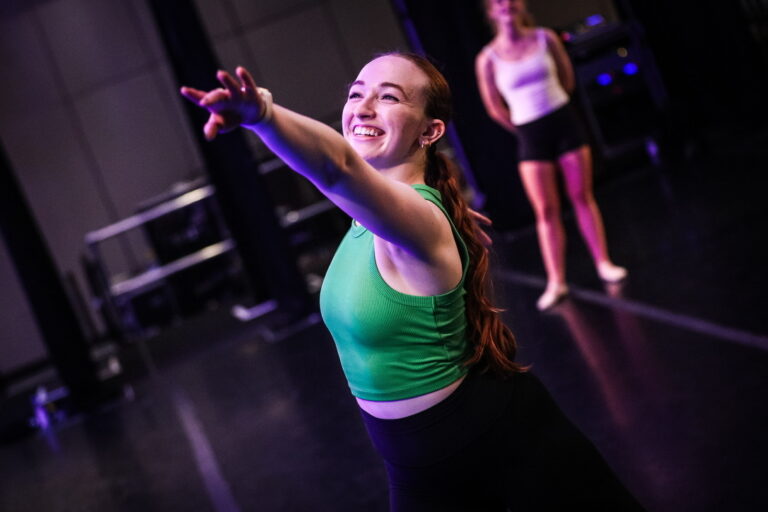 Dancer Makayla Ryan with her left arm raised and smiling.