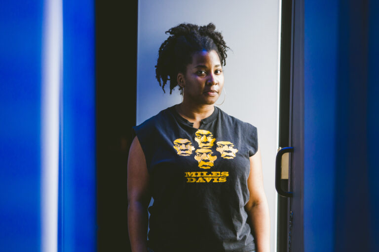 Melanie George wearing a black tshirt showing four yellow faces and text "Miles Davis"