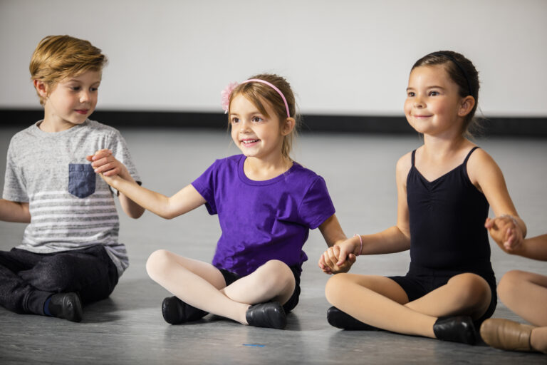Group of children holding hands in a dance studio.