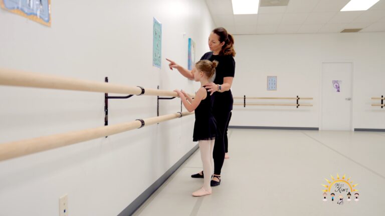 Dance educator Kim Black at the barre with a young student pointing at a picture on the wall.