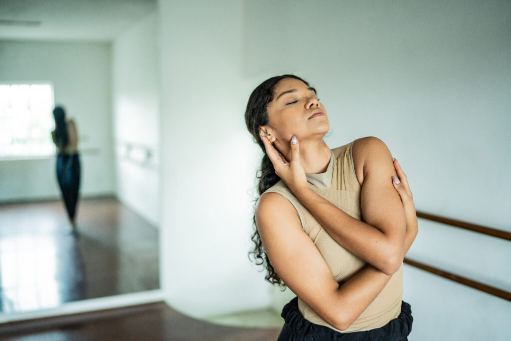 Woman dancing in a dance studio with arms wrapped around her body and eyes closed.