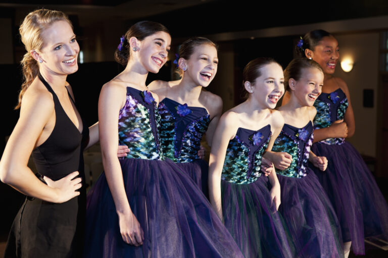 Teacher with group of young ballet dancers smiling in costume.