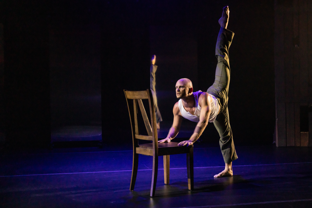 a male dancer performing a penche while leaning on a wooden chair