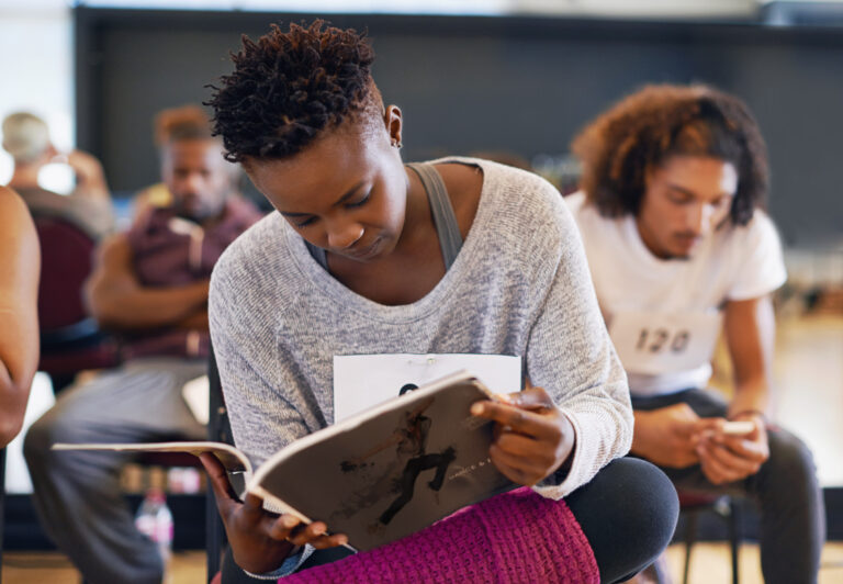 Young female dancer reading a dancing magazine while waiting for her audition.