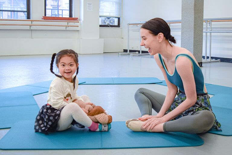 Mackenzie Fey smiling and seated on the floor in butterfly position with her student sitting facing her.