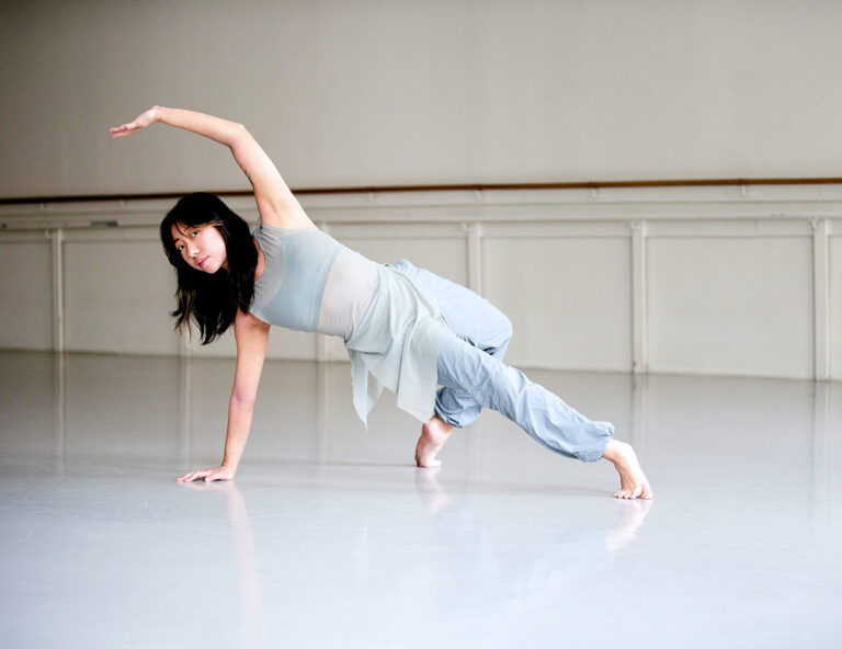 Dancer Vi Dolan in a one arm handstand with the other arm outstretched by her ear.