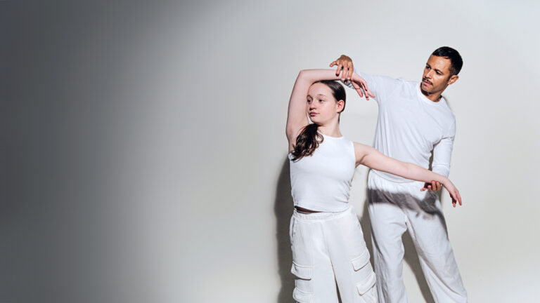 Dance instructor assisting a student both dressed in white.