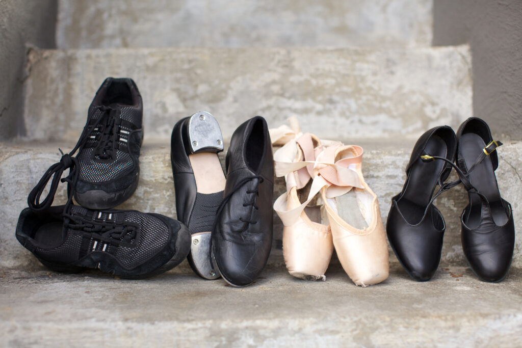 Closeup of a pair of jazz shoes, tap shoes, ballet pointe shoes, and character shoes resting on concrete steps.