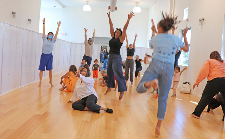 A mixed-ages group jumps and dances in a bright studio.