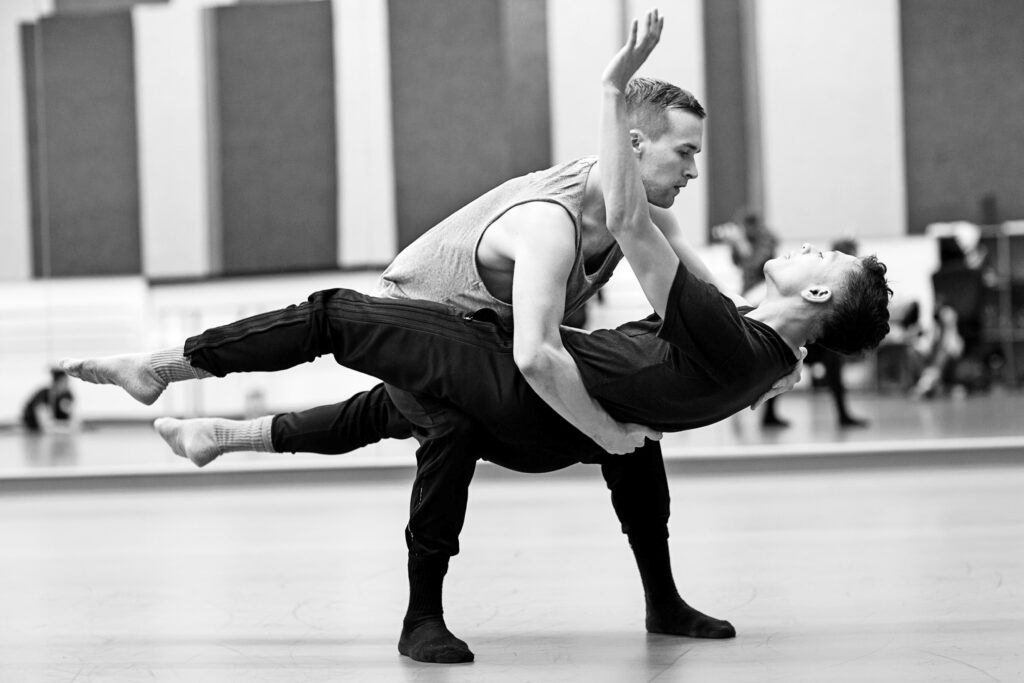 A black-and-white photo of two dancers, one cradling the other in a supported lift.