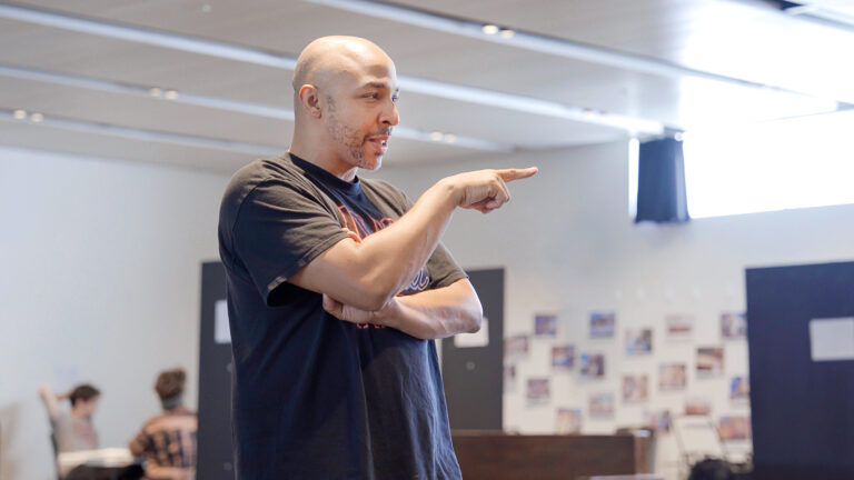 A bald man in a black t-shirt points while giving instructions.