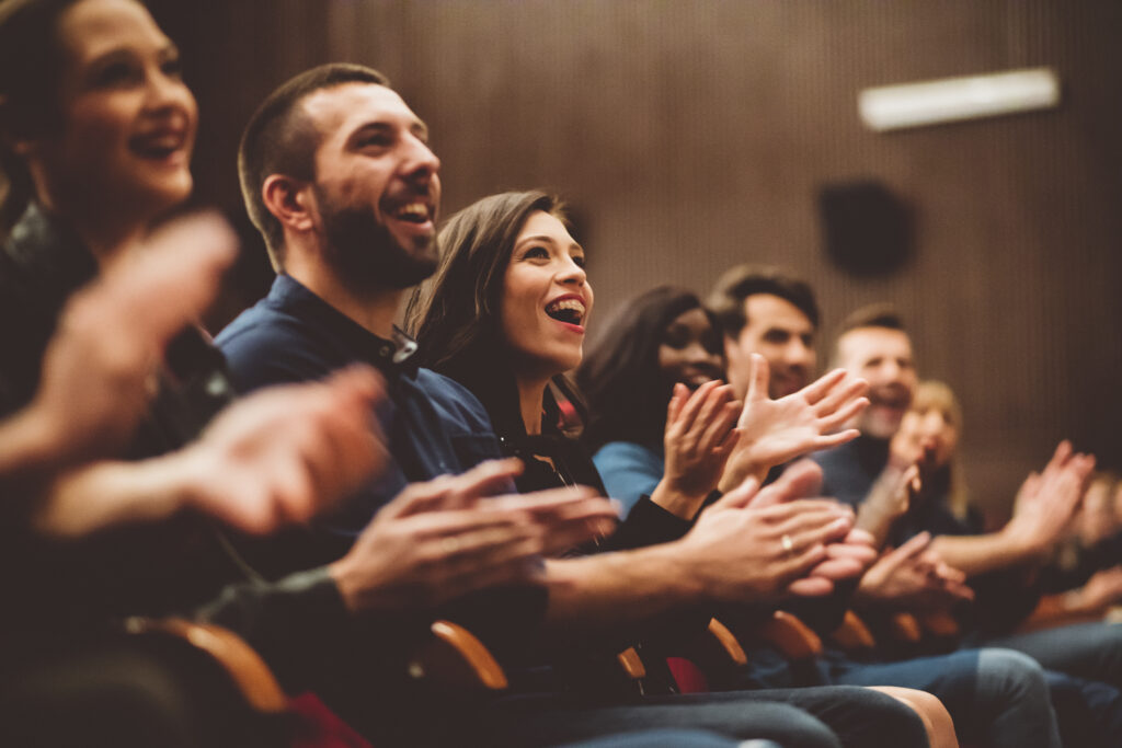A group of adults claps excitedly in an auditorium.