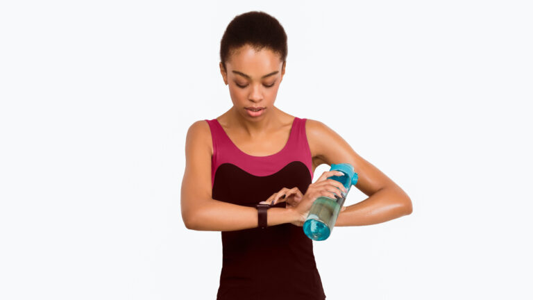 A ballet dancer with brown skin wearing a leotard checks her wrist fitness tracker.
