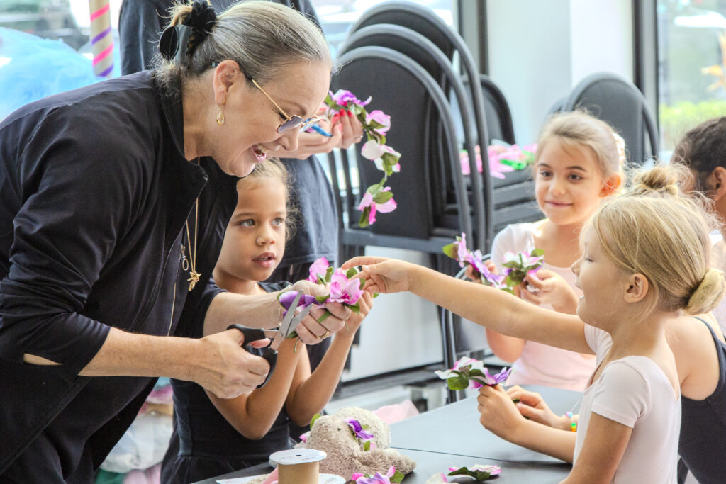 Diane Partington smiles widely as she helps a young dancer craft a flower crown.