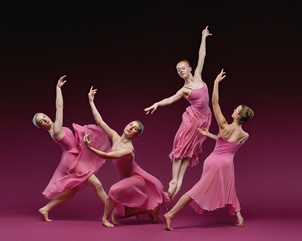 Four ballet dancers wearing pink dresses strike different poses against an ombre pink-black backdrop.