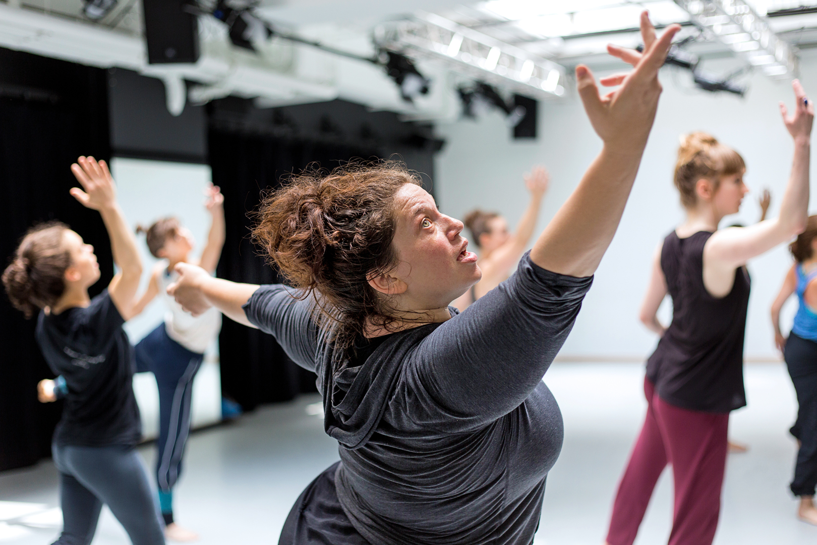 Alexandra Beller wearing a grey top, arms outstretched and looking upward.