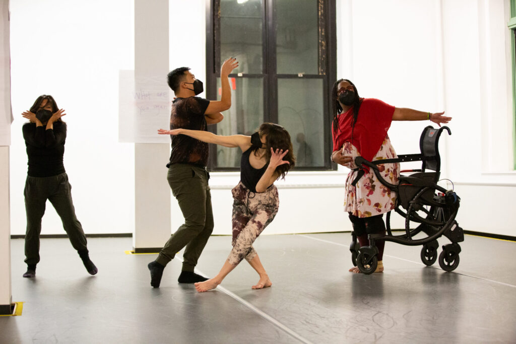 Group of dancers holding various poses including one standing against a wheelchair.