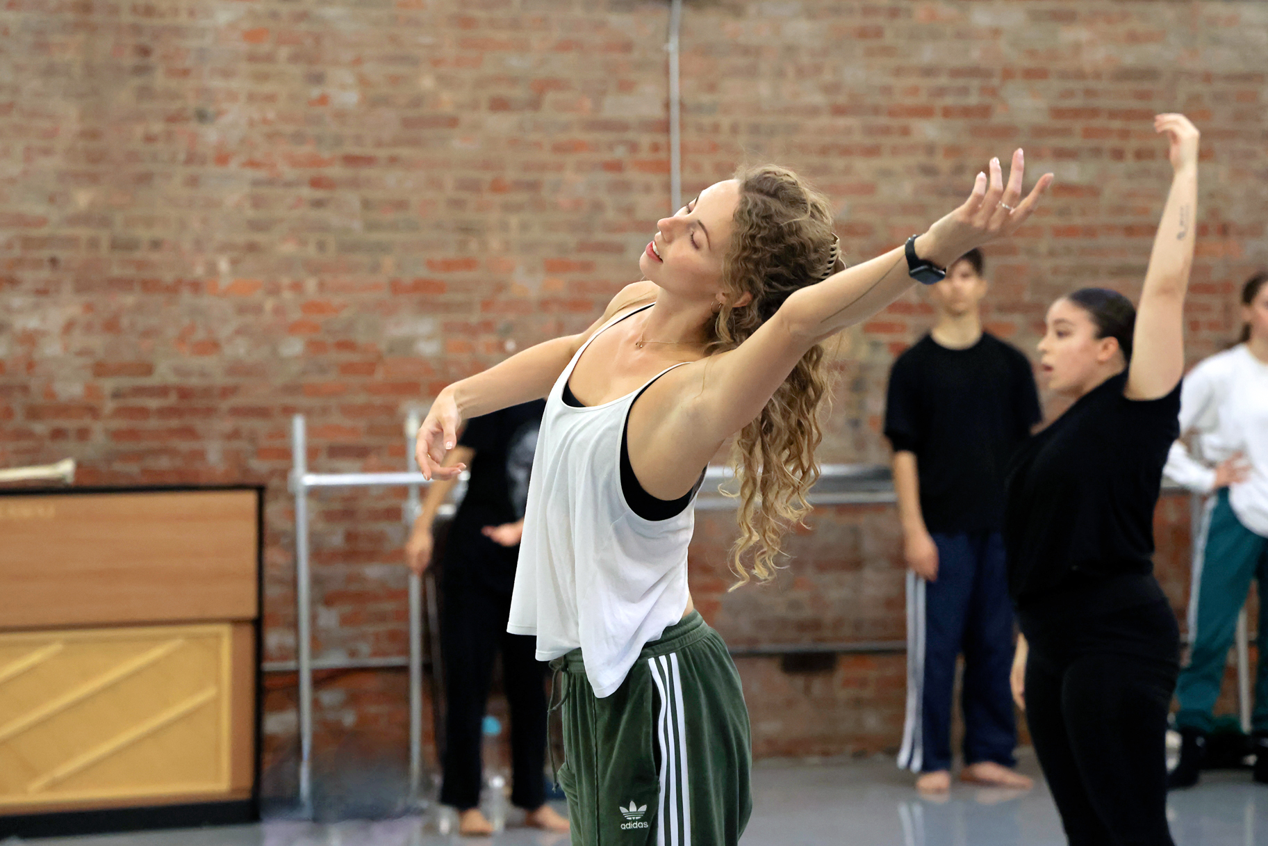 Francesca Dominguez teaching a class wearing a white vest and green adidas track pants. She leans sideways with one arm extended.