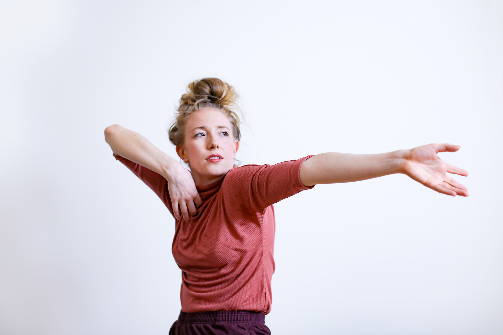 Annie Rigney in a dark rose tshirt with one arm outstretched and the other folded against her chest. She looks sideways.