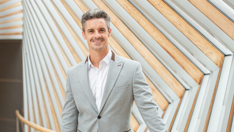 Iain Mackay, artistic director of The Royal Ballet School pictured from the torso up, wearing a grey suit and white shirt.