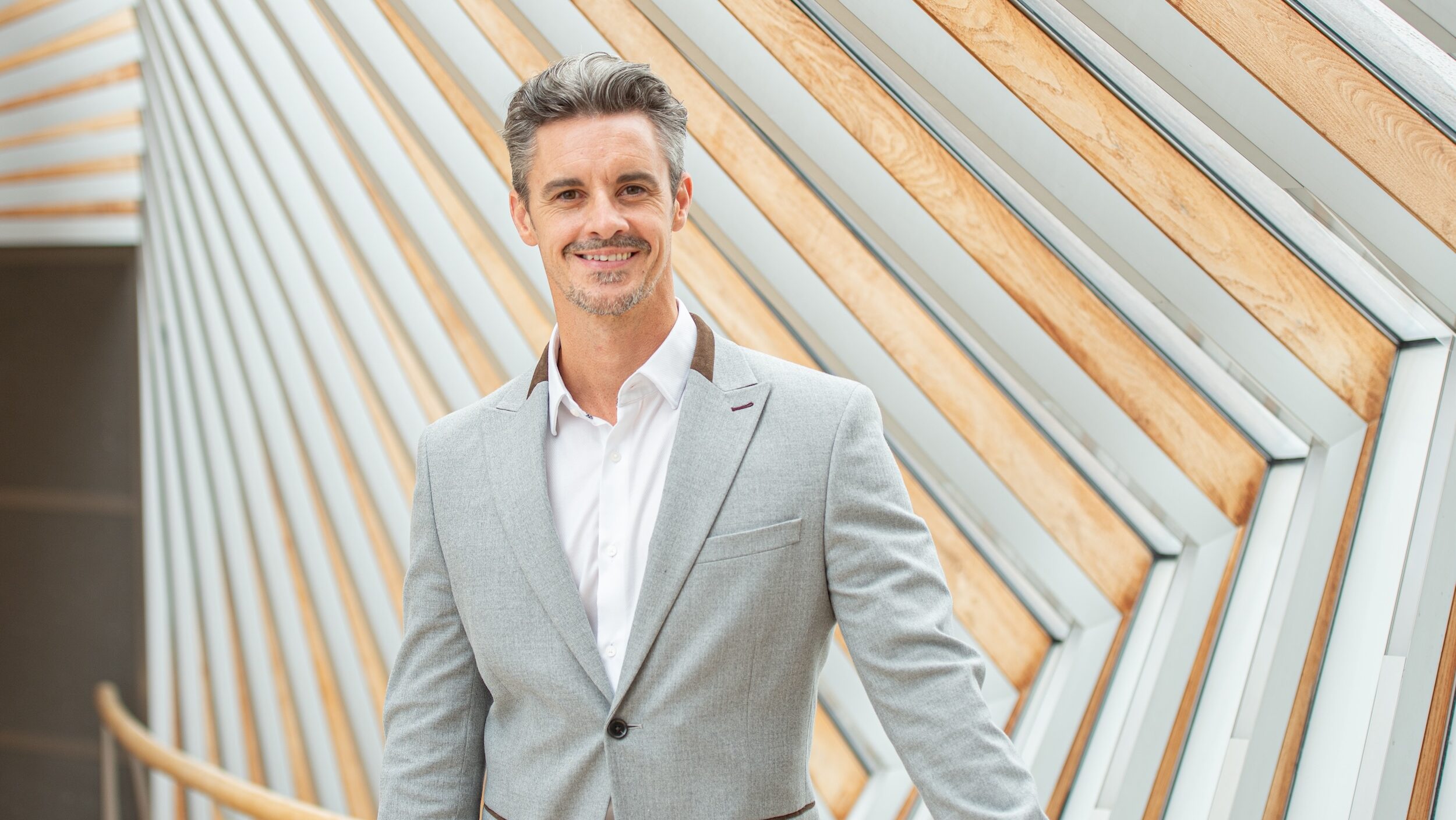Iain Mackay, artistic director of The Royal Ballet School pictured from the torso up, wearing a grey suit and white shirt.