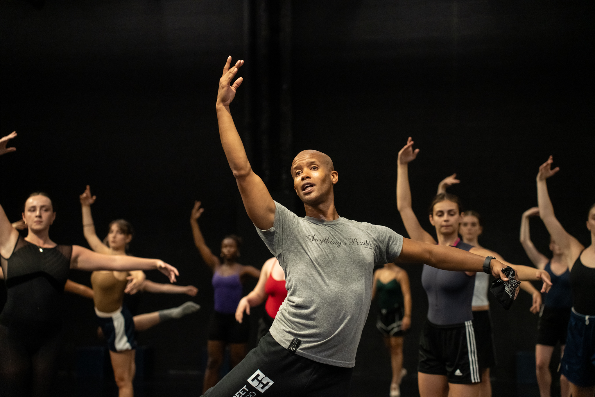 Jonathan Alsberry teaching a class wearing a grey tshirt and black pants with arms held in open fifth position.