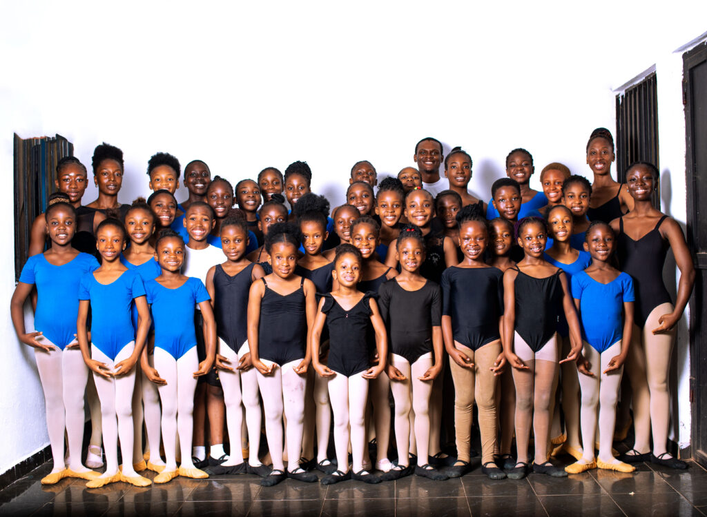 A group of young Nigerian dancers dressed in black and blue leotards, tights, and ballet shoes.